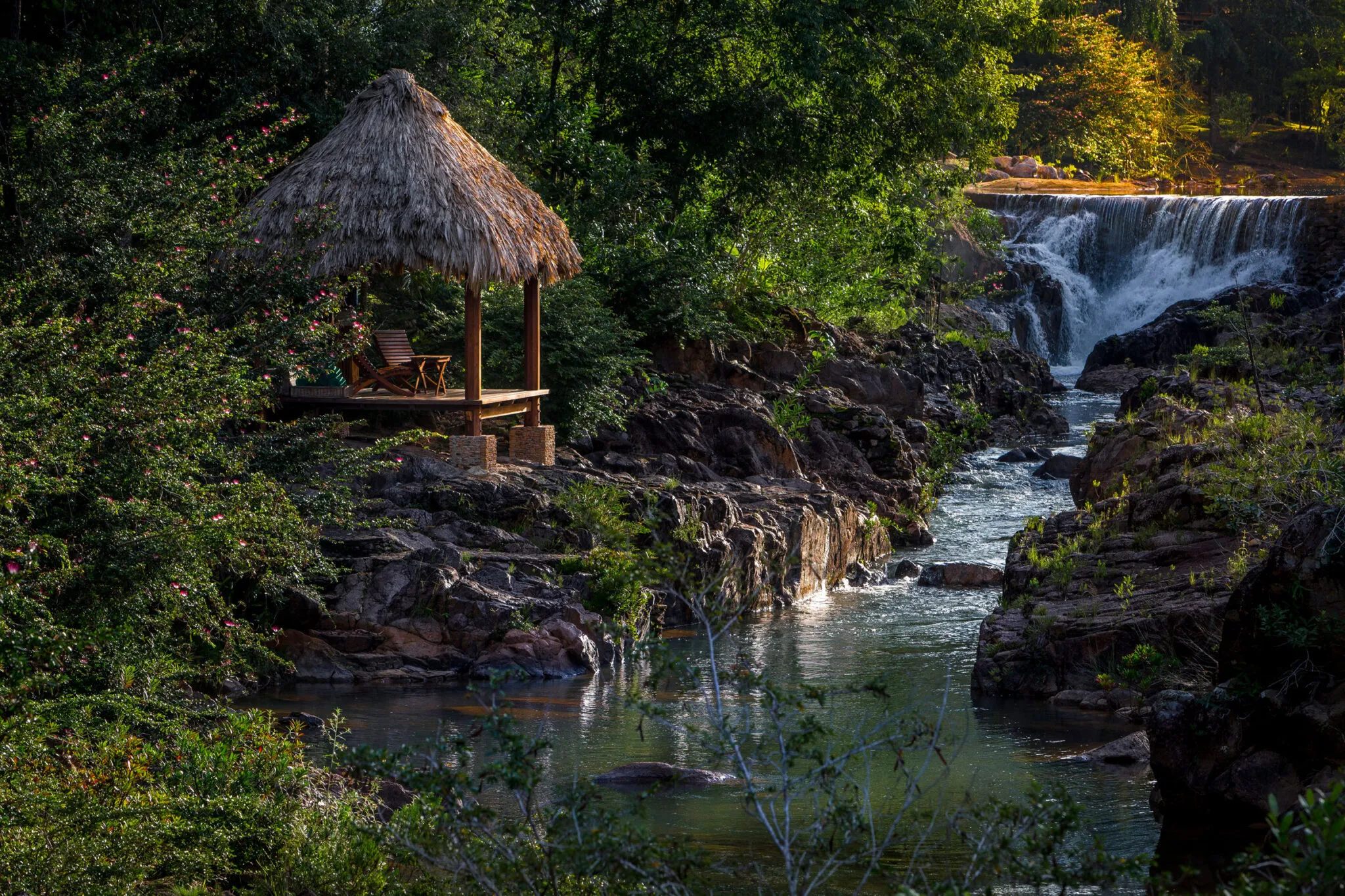 Outdoor lounge chairs next to a river with a waterfall