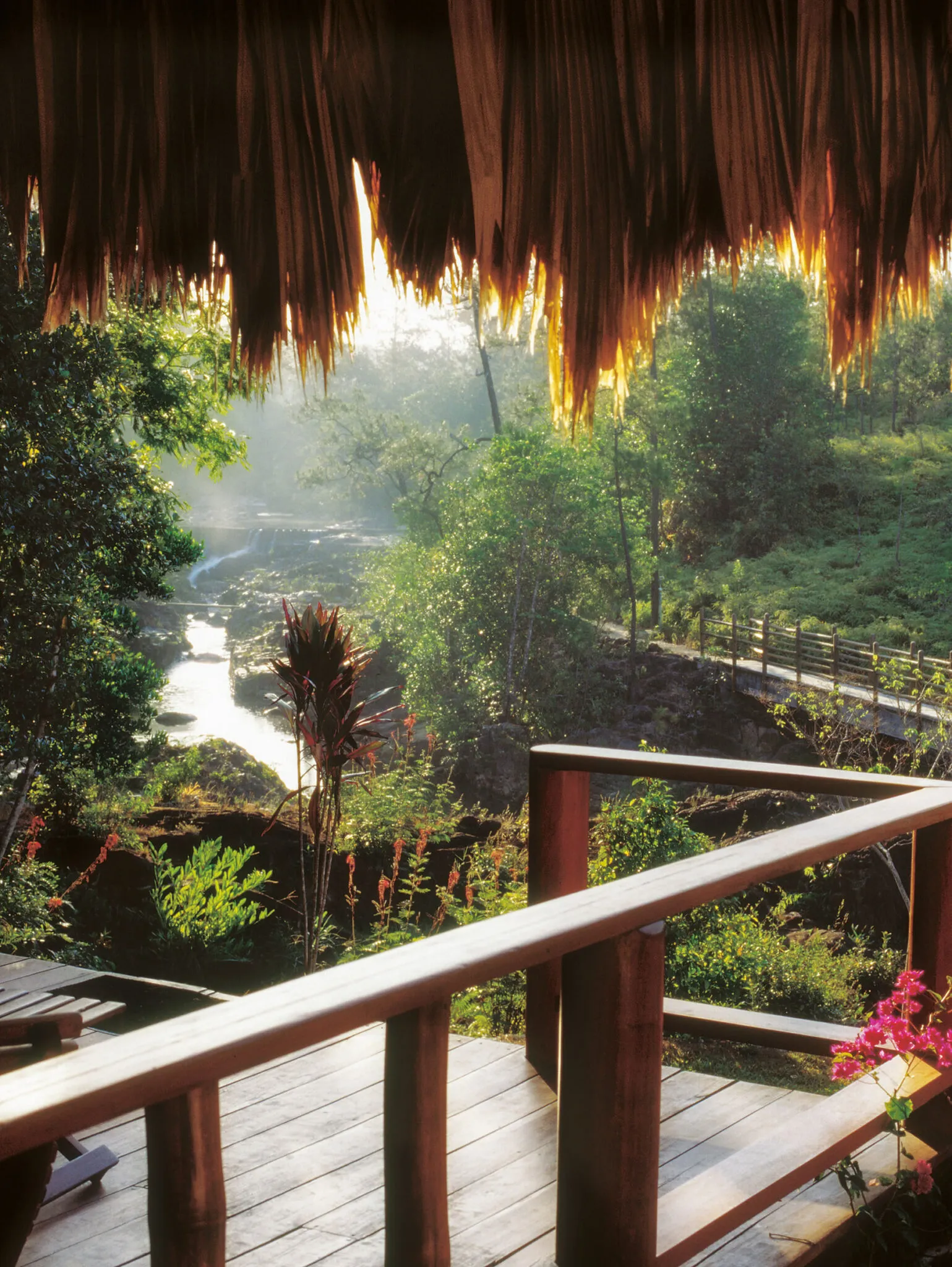 A wooden deck with a view of the water and a small bridge