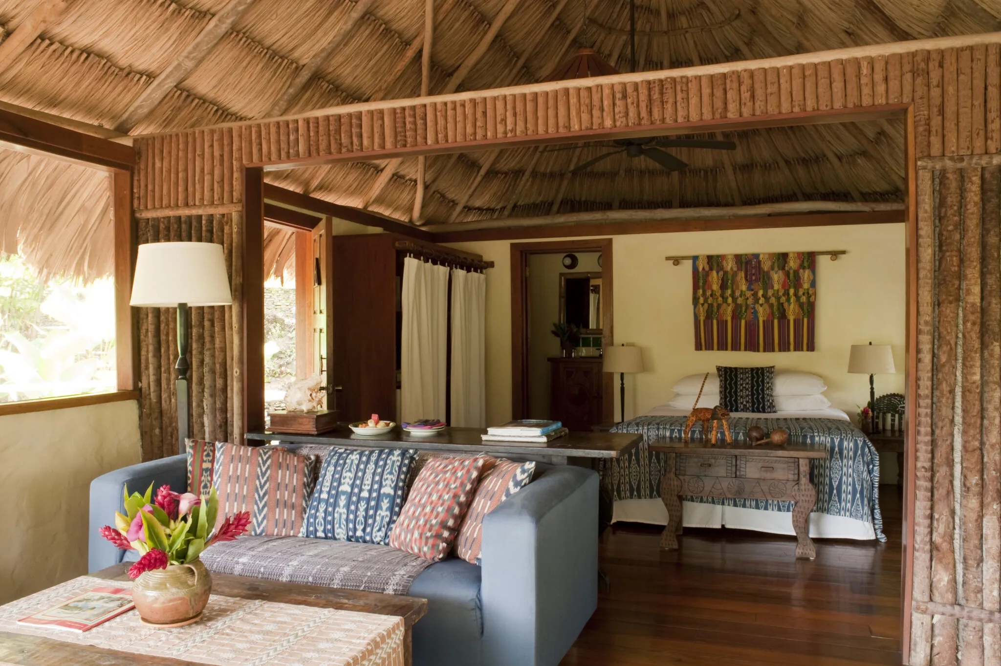 Honeymoon Cabana interior with living area sofa and a double bed under a thatched roof