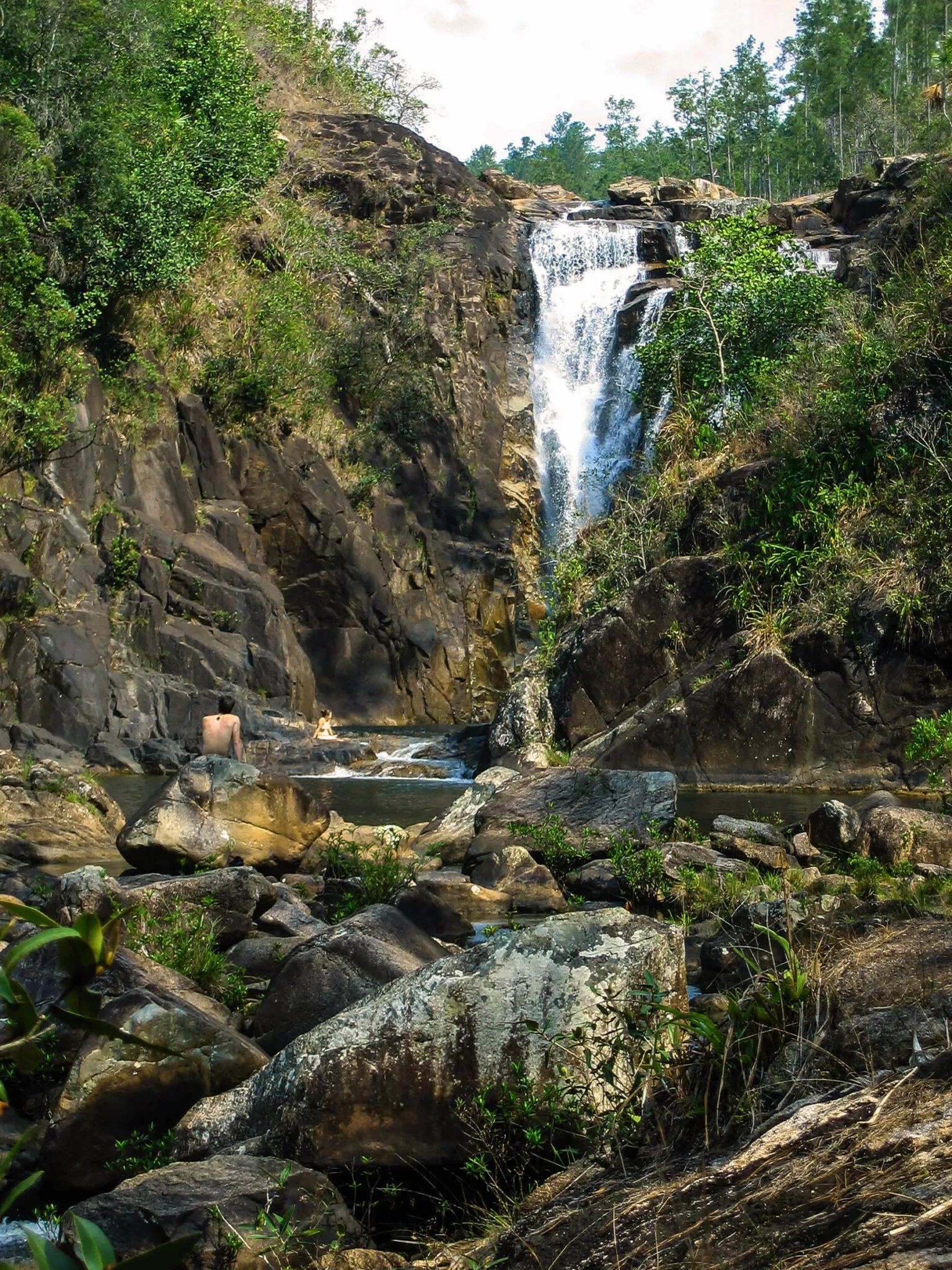 A couple relaxes on the rocks near a waterfall