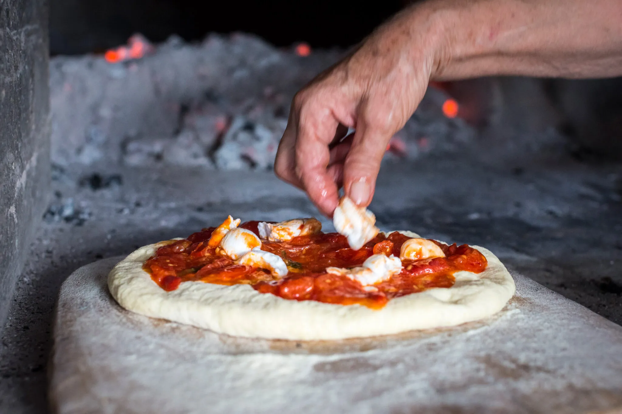 A man tops a pizza with mozzarella balls