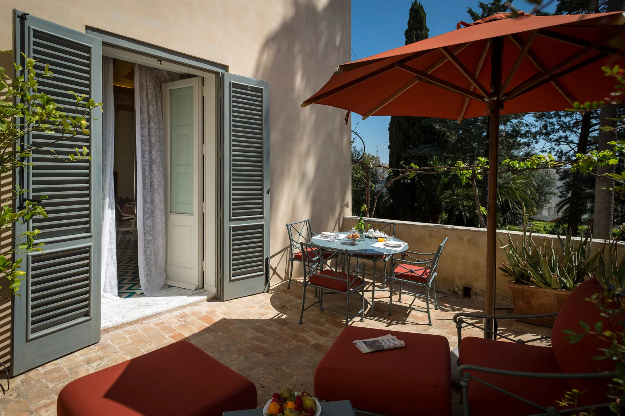 Private balcony with red cushioned chairs under and umbrella and dining table