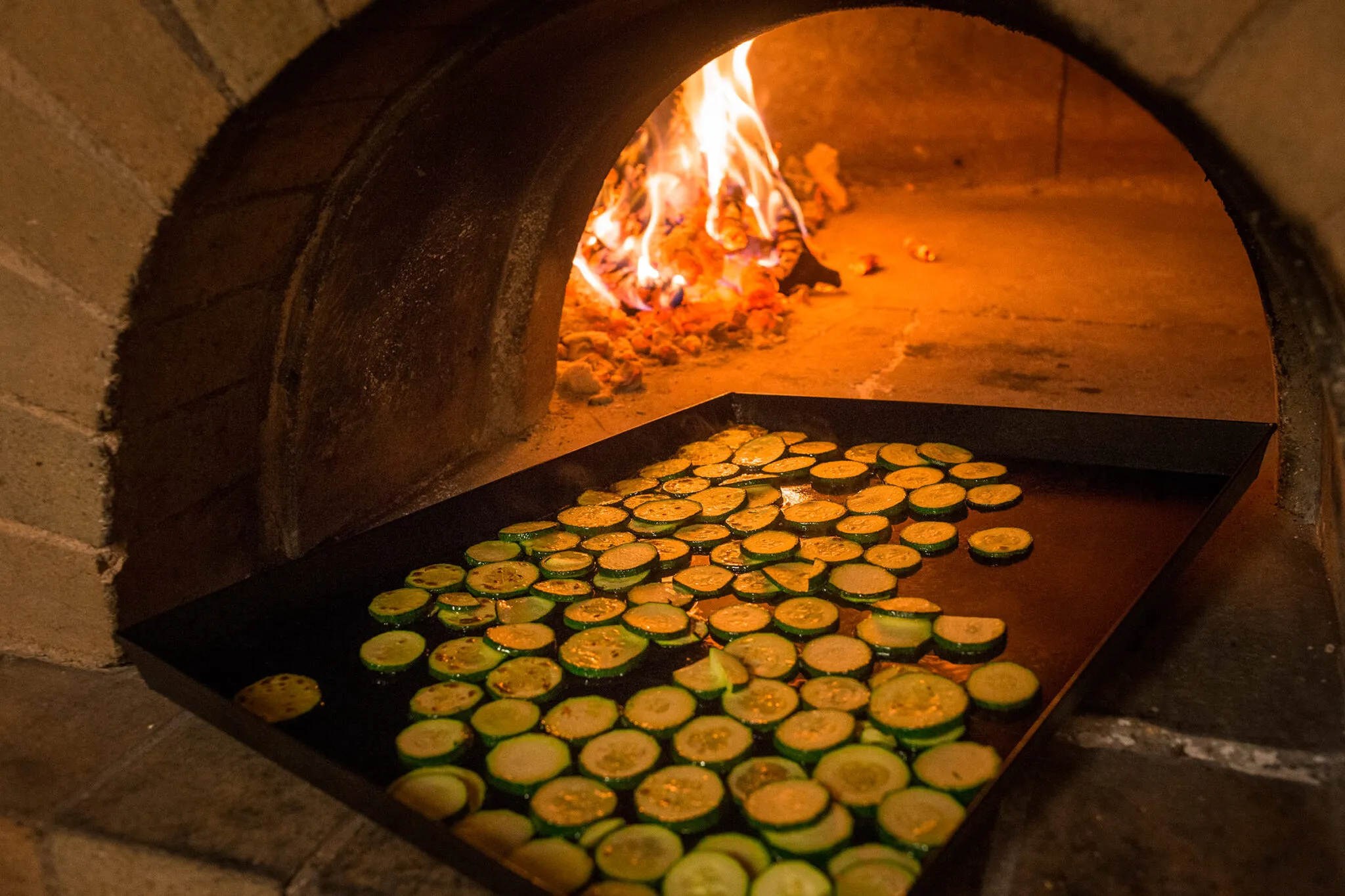 A tray of sliced zucchini going into a brick oven