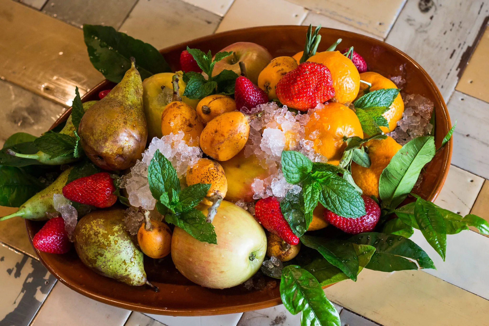 A bowl of fresh strawberries, pears, apples and herbs