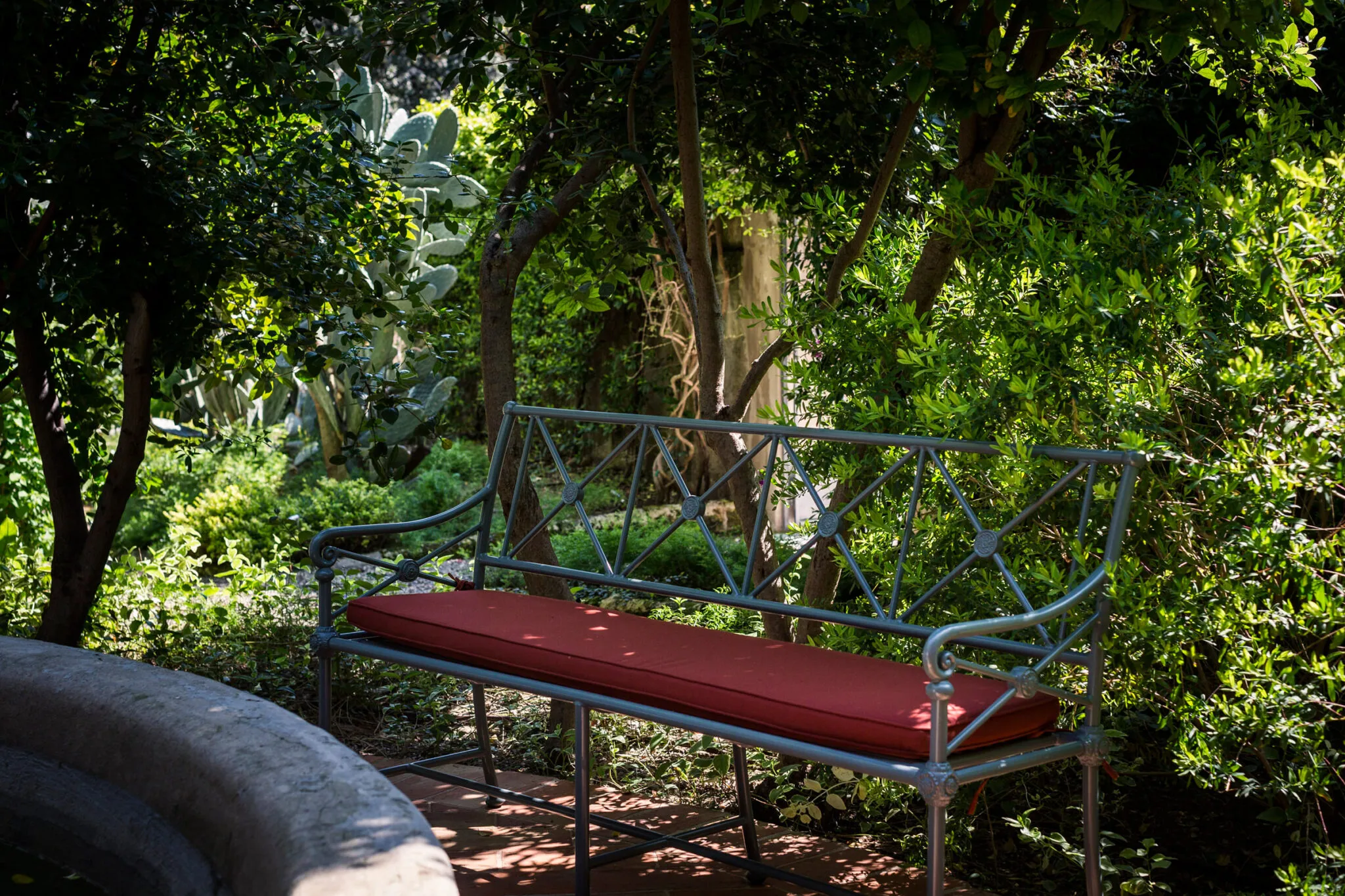 A wrought iron bench with a red cushion next to fountain