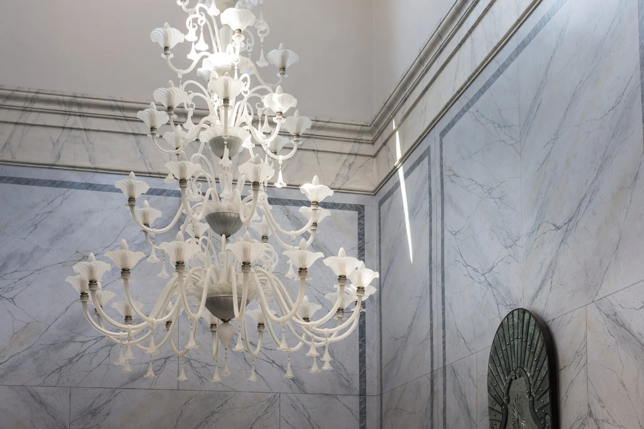 A white glass chandelier hangs in front of marble walls