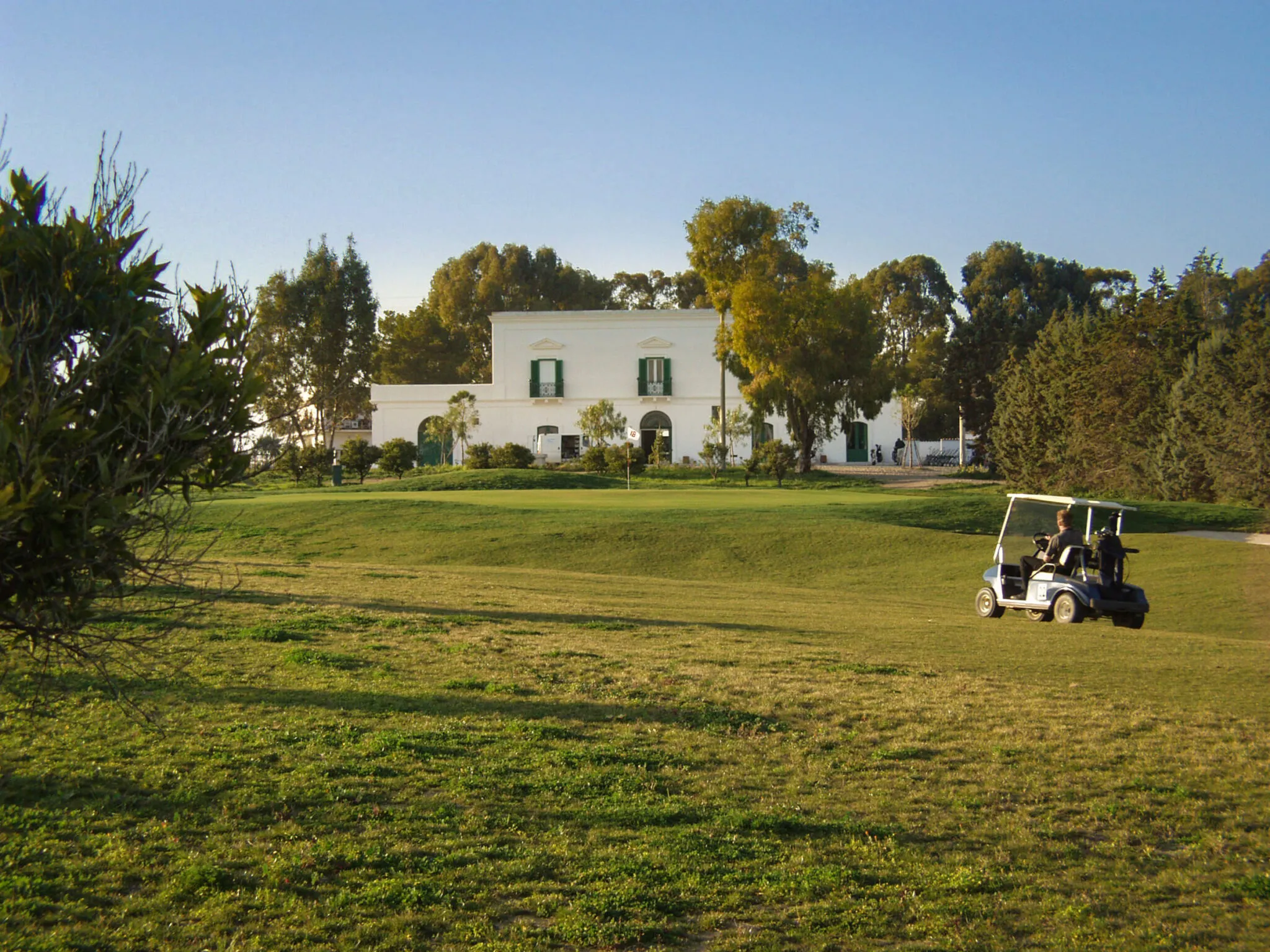 A golf cart on the green in front of a clubhouse