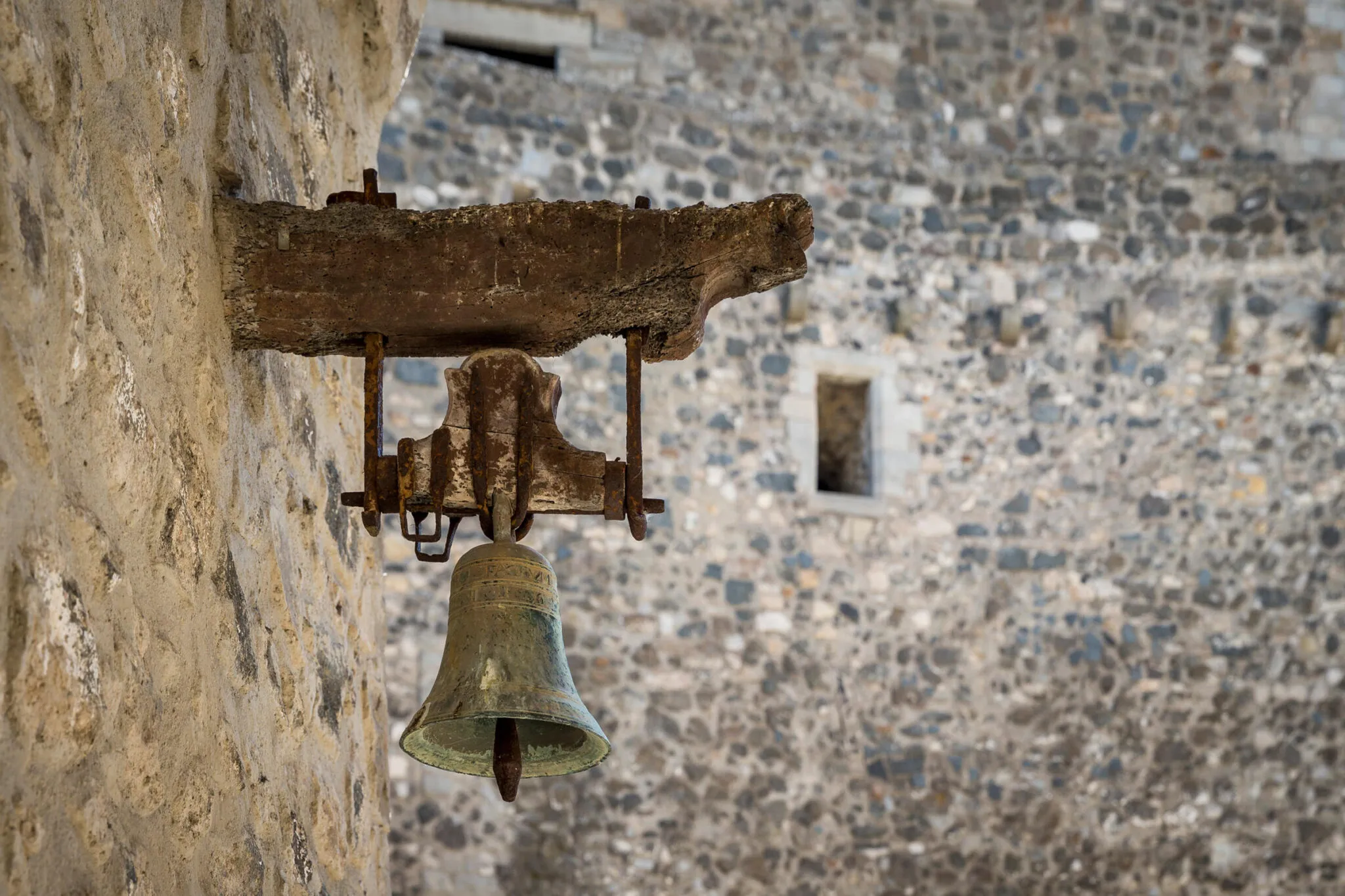 Detail of a bell hanging on a stone wall