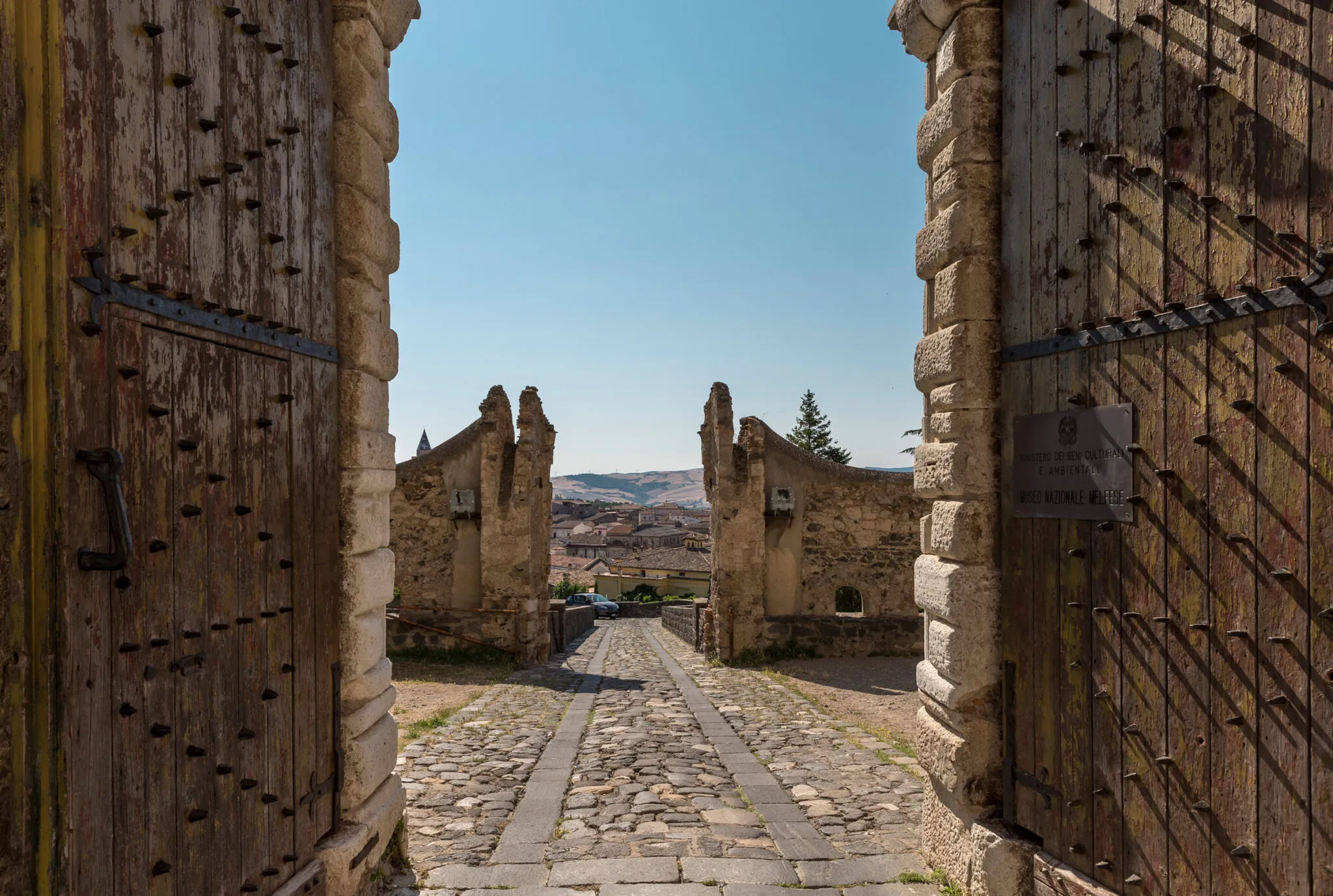 A stone walkway between gates and buildings at Melfi