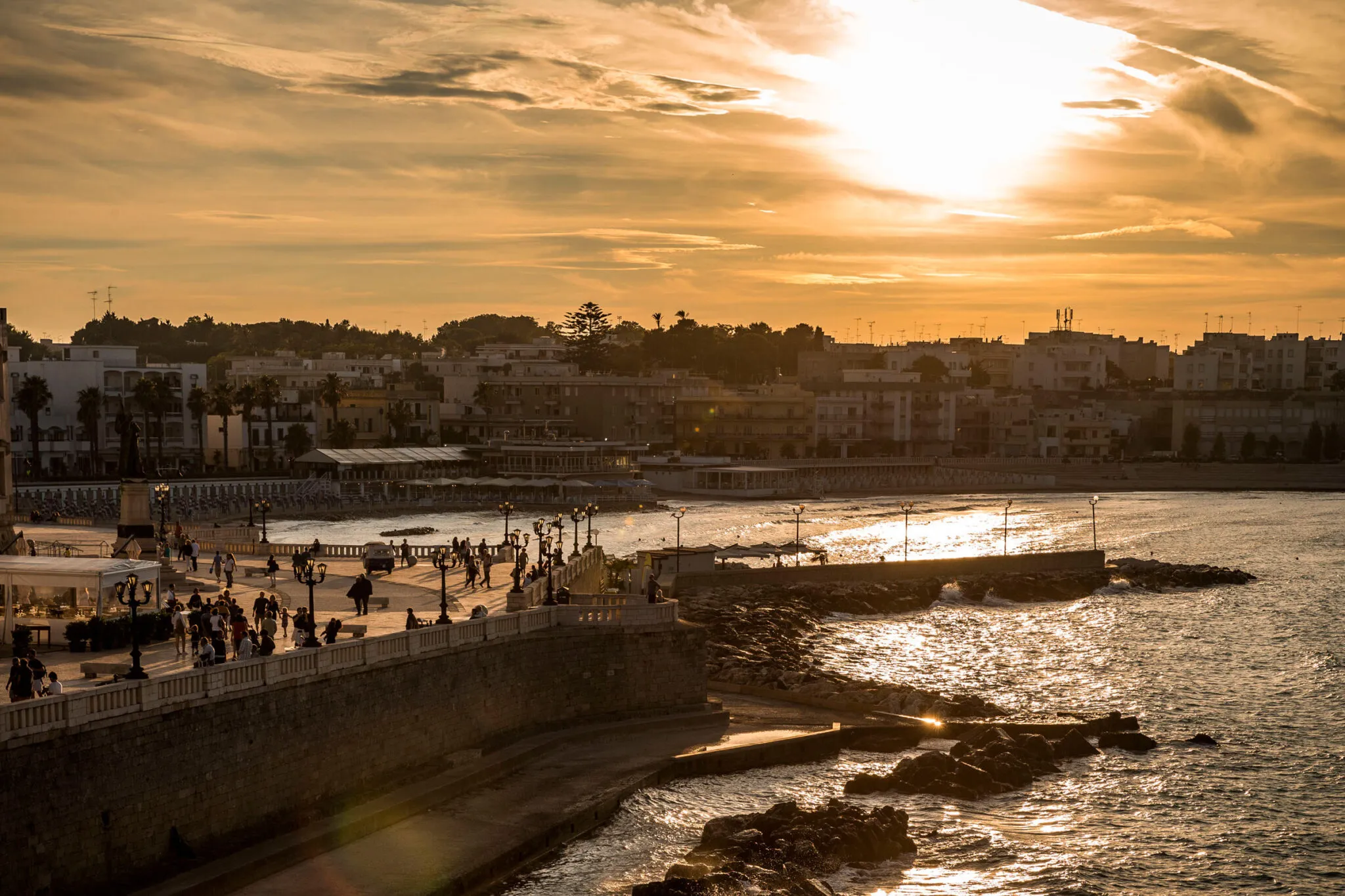 People on a promenade by the sea at sunset