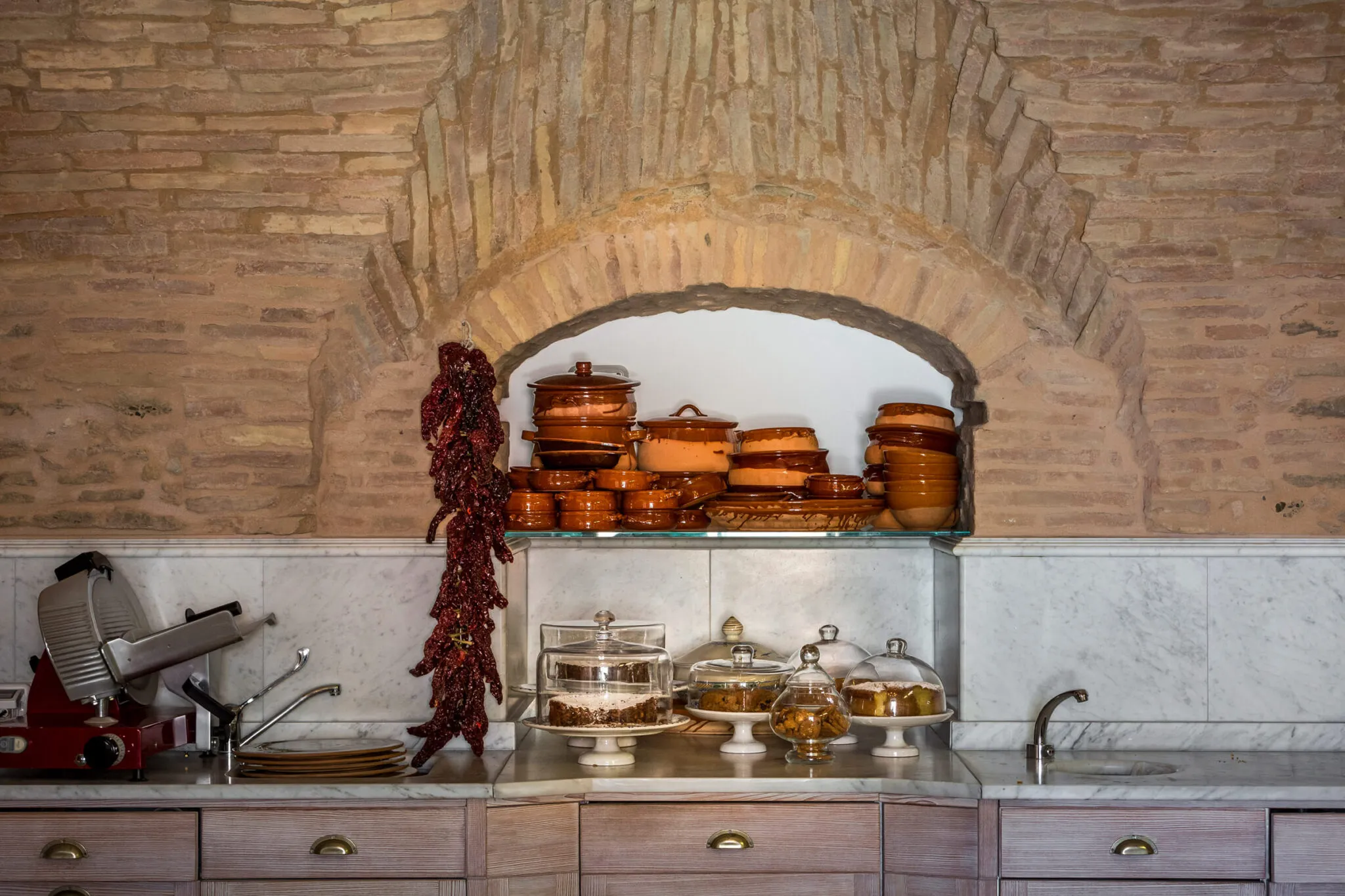 Ceramic dishes stacked in a brick wall above a marble countertop with pastries