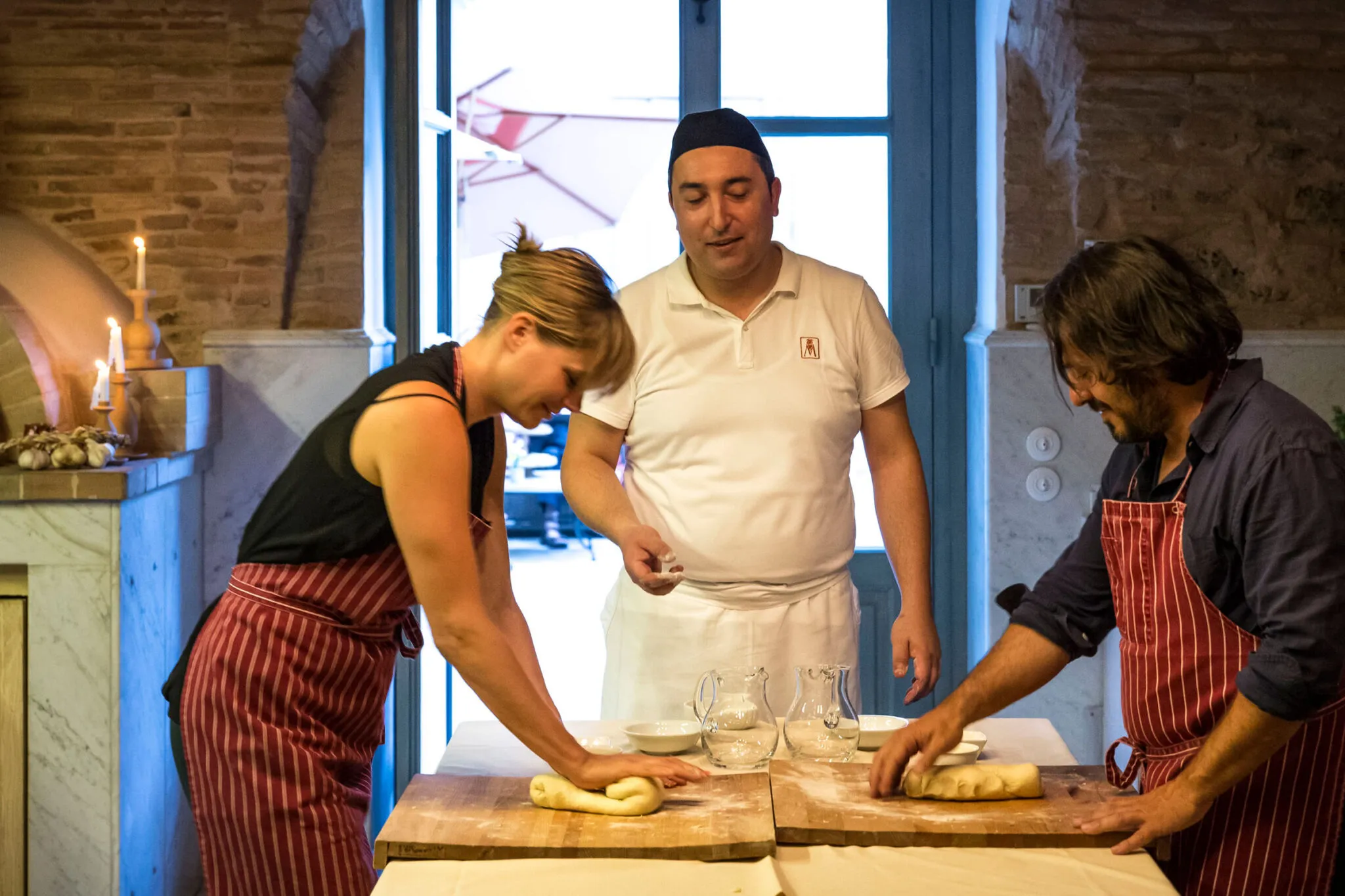 A chef helps a man and woman prepare pizza dough