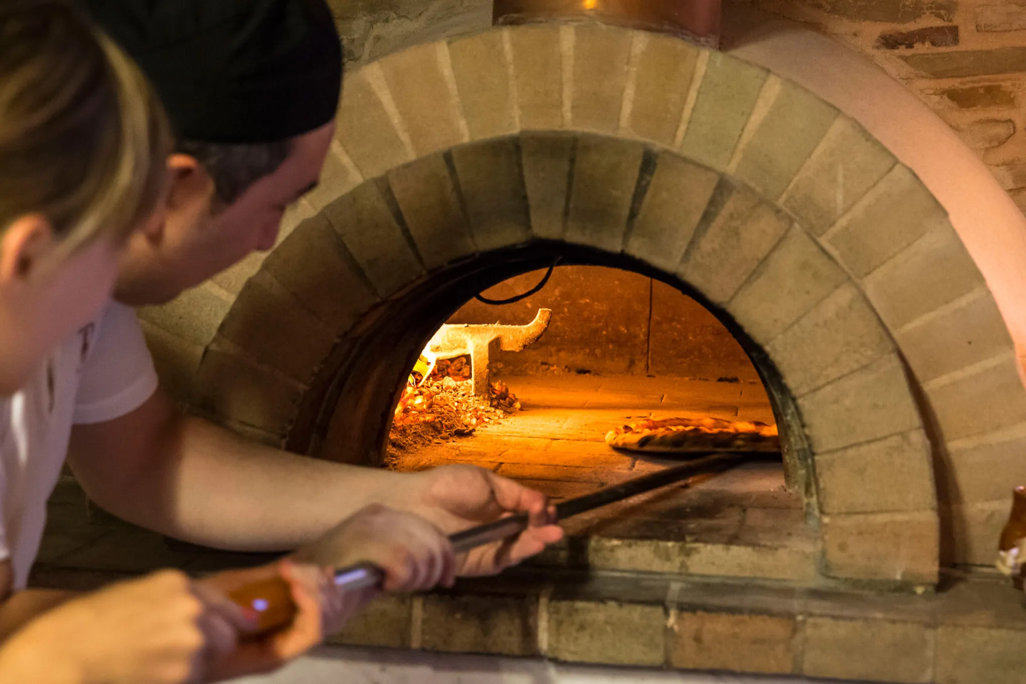 A chef slides a pizza into a wood-fired brick oven