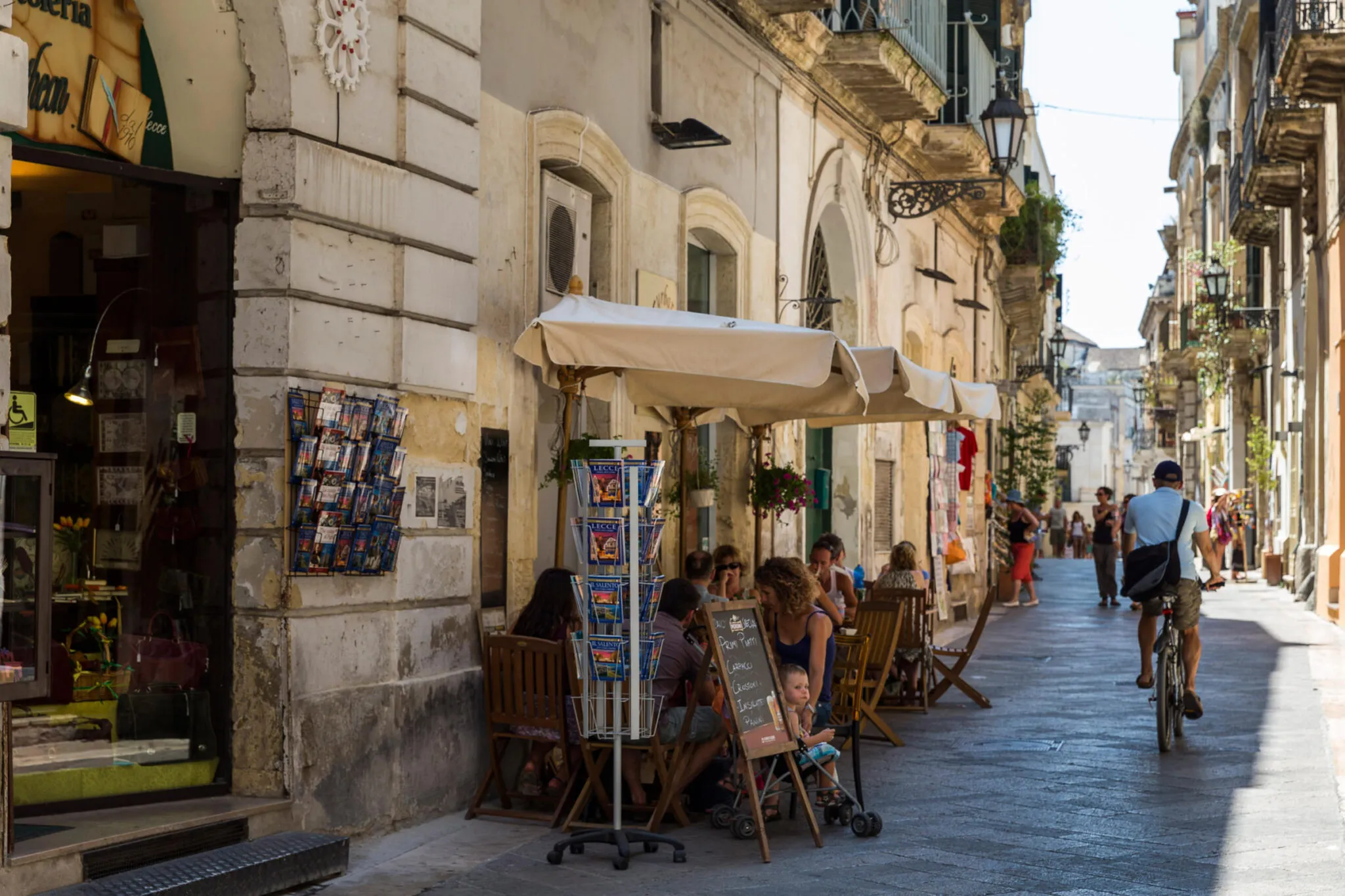 People eat outside of a cafe while a man rides past on a bicycle