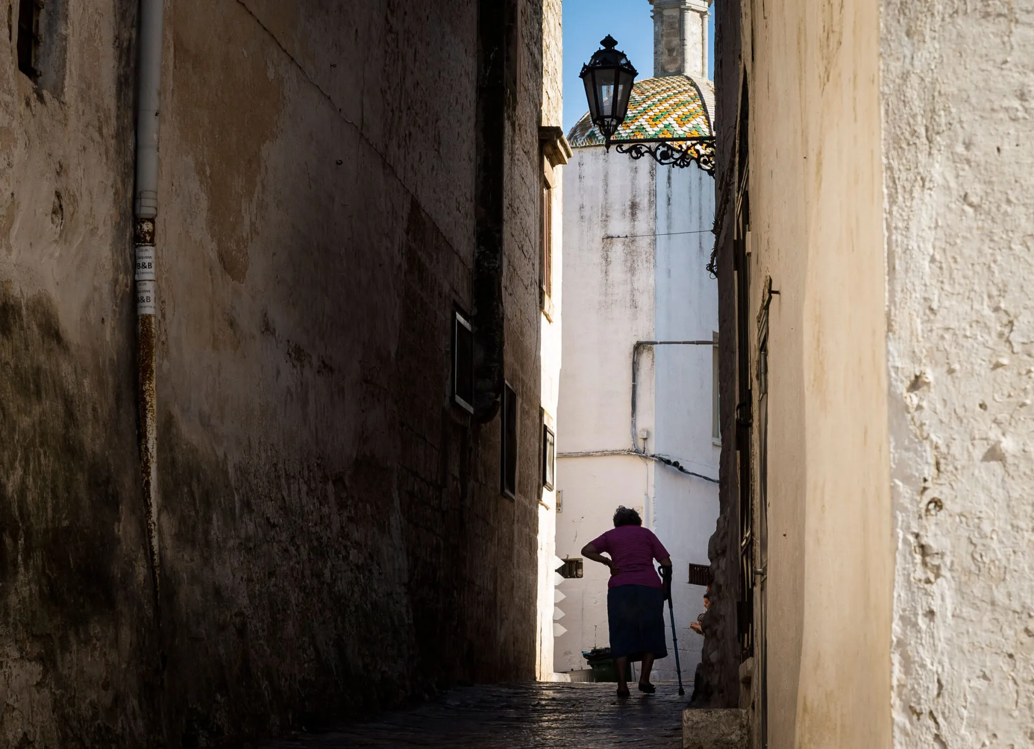 An older woman uses a cane as she walks between buildings