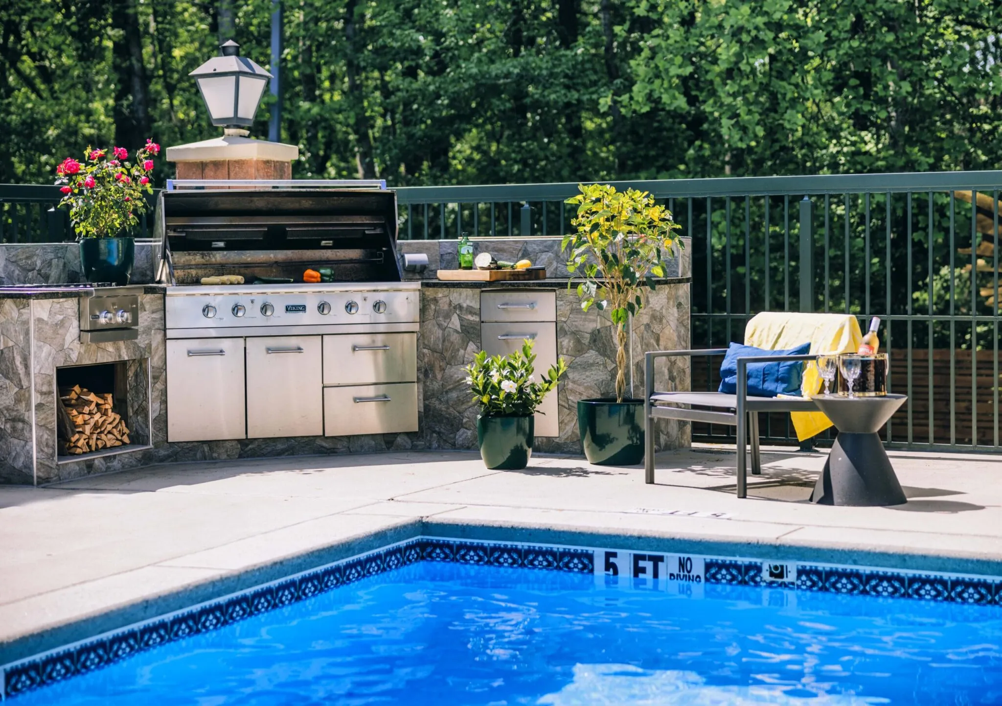 A grill and lounge chair sit next to a clear blue swimming pool.