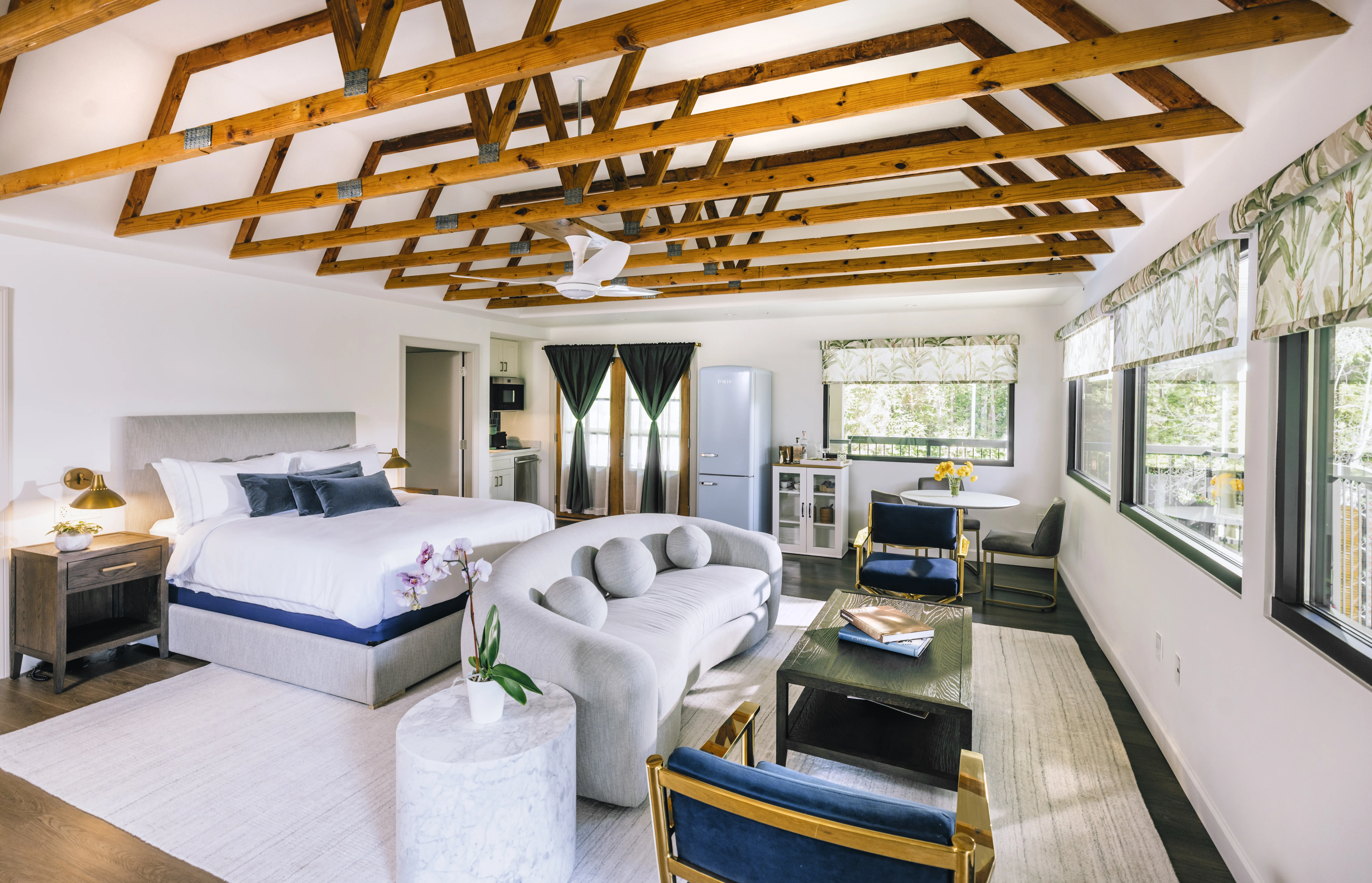 A hotel room with a large bed behind a living area, underneath a wood beam ceiling.