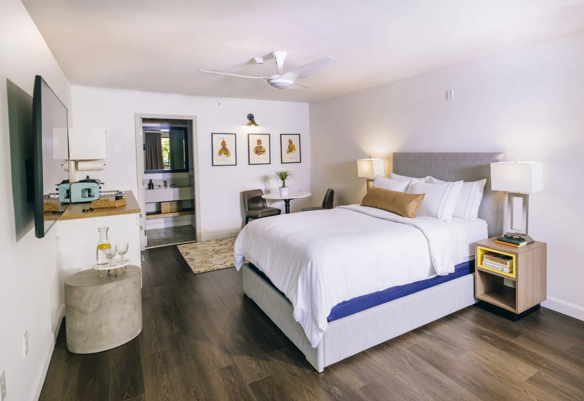 A hotel suite with wood floors and a large bed with white linens.