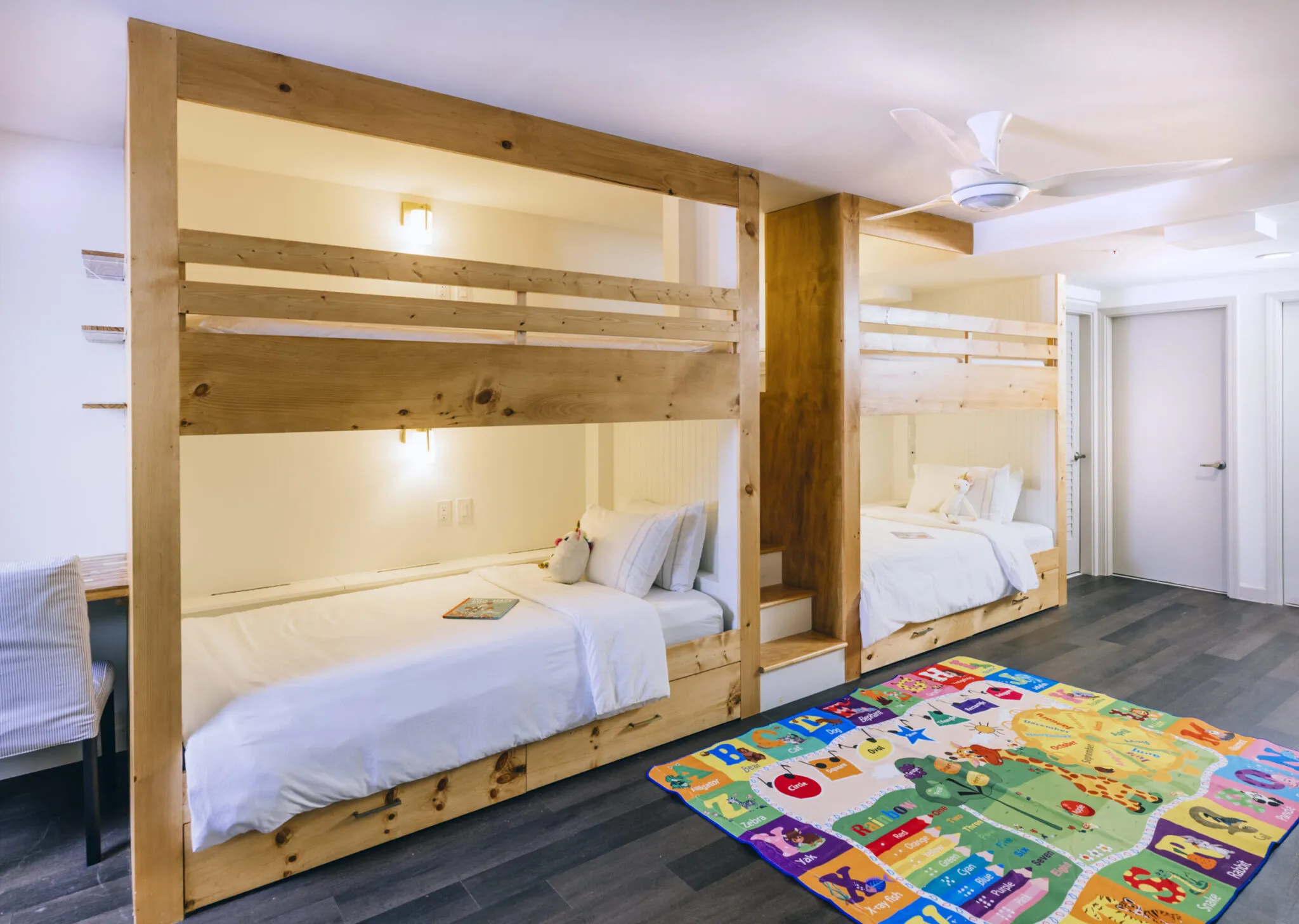 A room with two sets of wooden bunk beds and a colorful carpet.